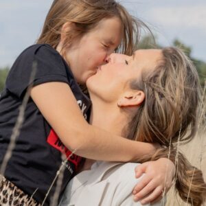 Moeder geeft dochter een kus in een teder moment, beeld van liefde en veilige hechting.